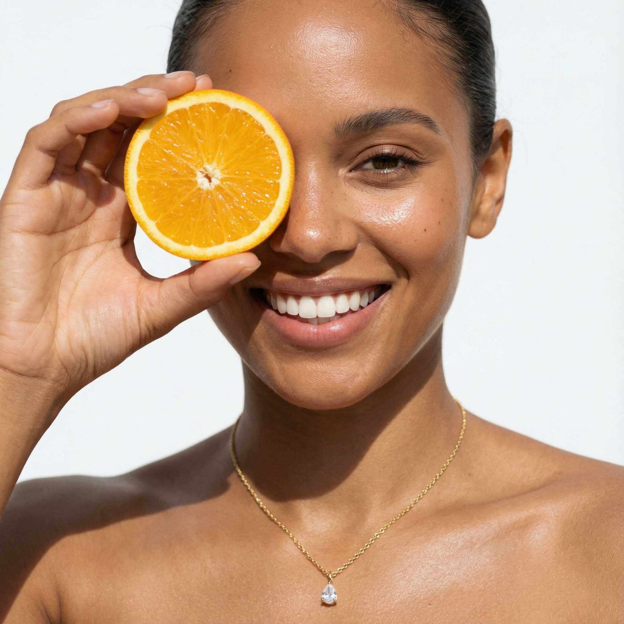 Astra Teardrop Necklace by Brother & Sisters worn by a smiling woman holding an orange slice.