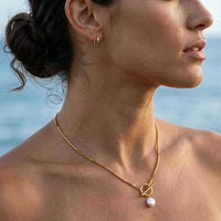 Thumbnail for Woman wearing La Isla Pearl Toggle Necklace by Brother & Sisters, featuring a gold clasp and freshwater pearl.