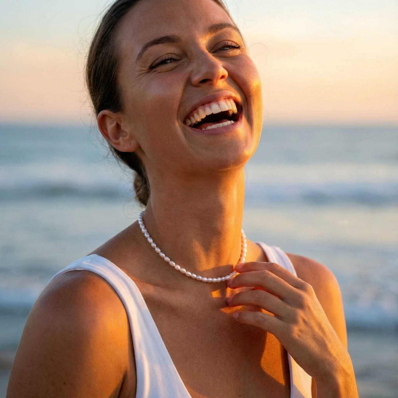 Joyful bride wearing pearl choker at golden hour beach — bridal pearl necklace for wedding day