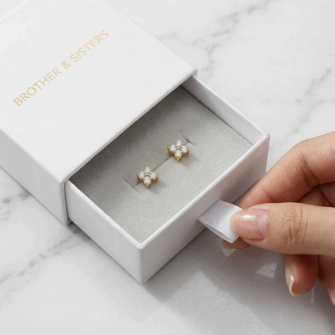 Crystal Flower Stud Earrings in a white box by Brother & Sisters, showcasing delicate four-leaf design and sparkle.