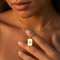 Thumbnail for Starlight Pendant Necklace worn by a woman, featuring a gold tag pendant with a starburst and zirconia stone, Brother & Sisters.
