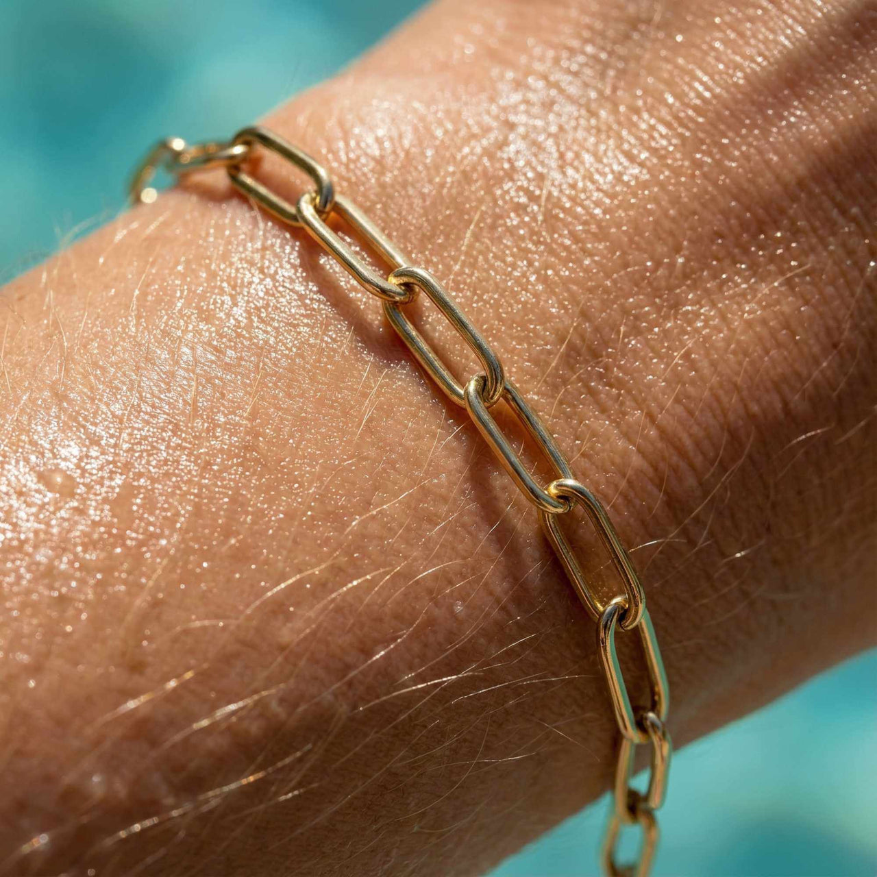 Close-up of a hand wearing a Paperclip Chain Bracelet by Brother & Sisters, showcasing its sleek gold links.