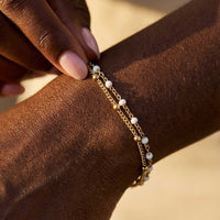 Thumbnail for Close-up of a model wearing the Double White Bracelet by Brother & Sisters, featuring gold links and white enamel beads.