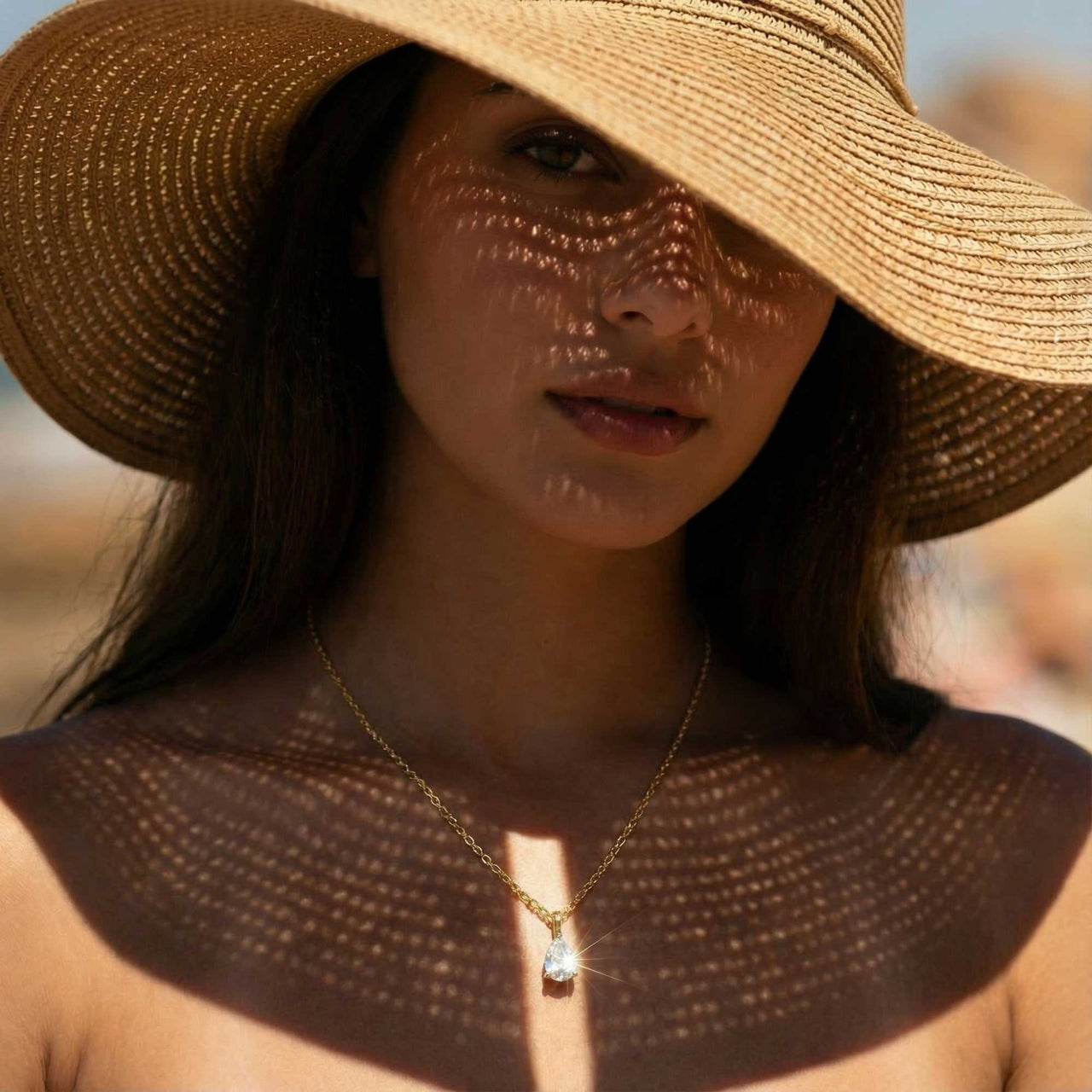 Astra Teardrop Necklace featuring a shimmering teardrop-cut stone worn by a model in a sun hat.