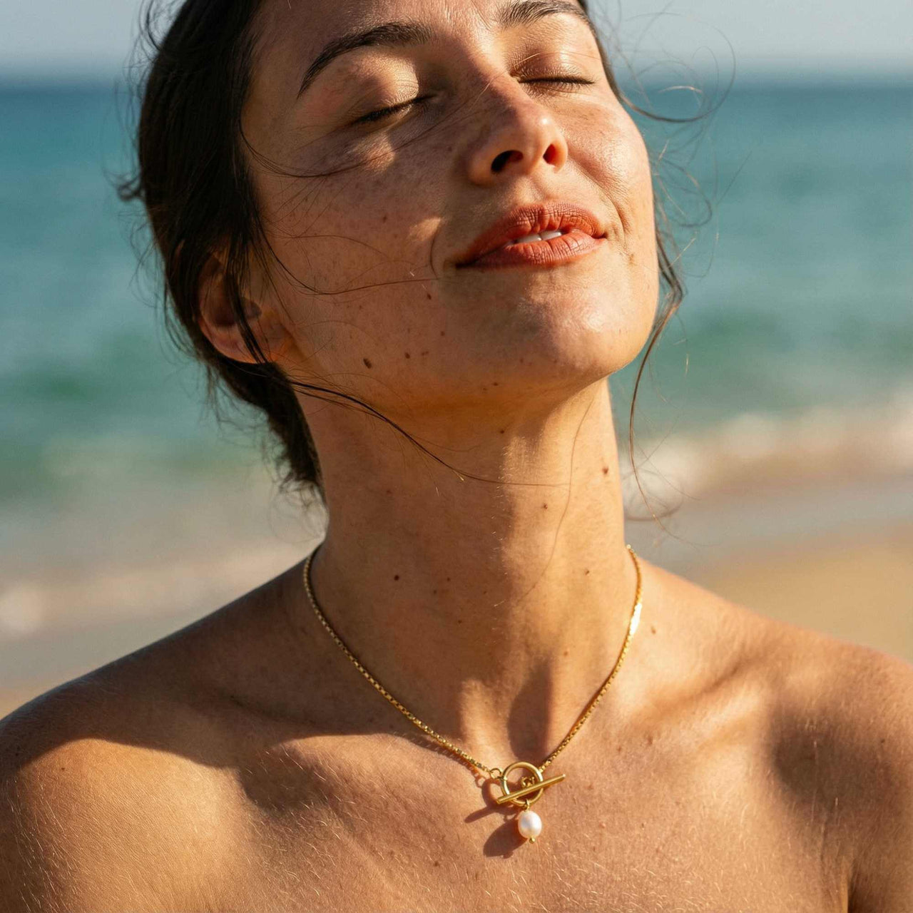 Model wearing La Isla Pearl Toggle Necklace by Brother & Sisters on the beach, showcasing its unique sculptural clasp and pearl detail.