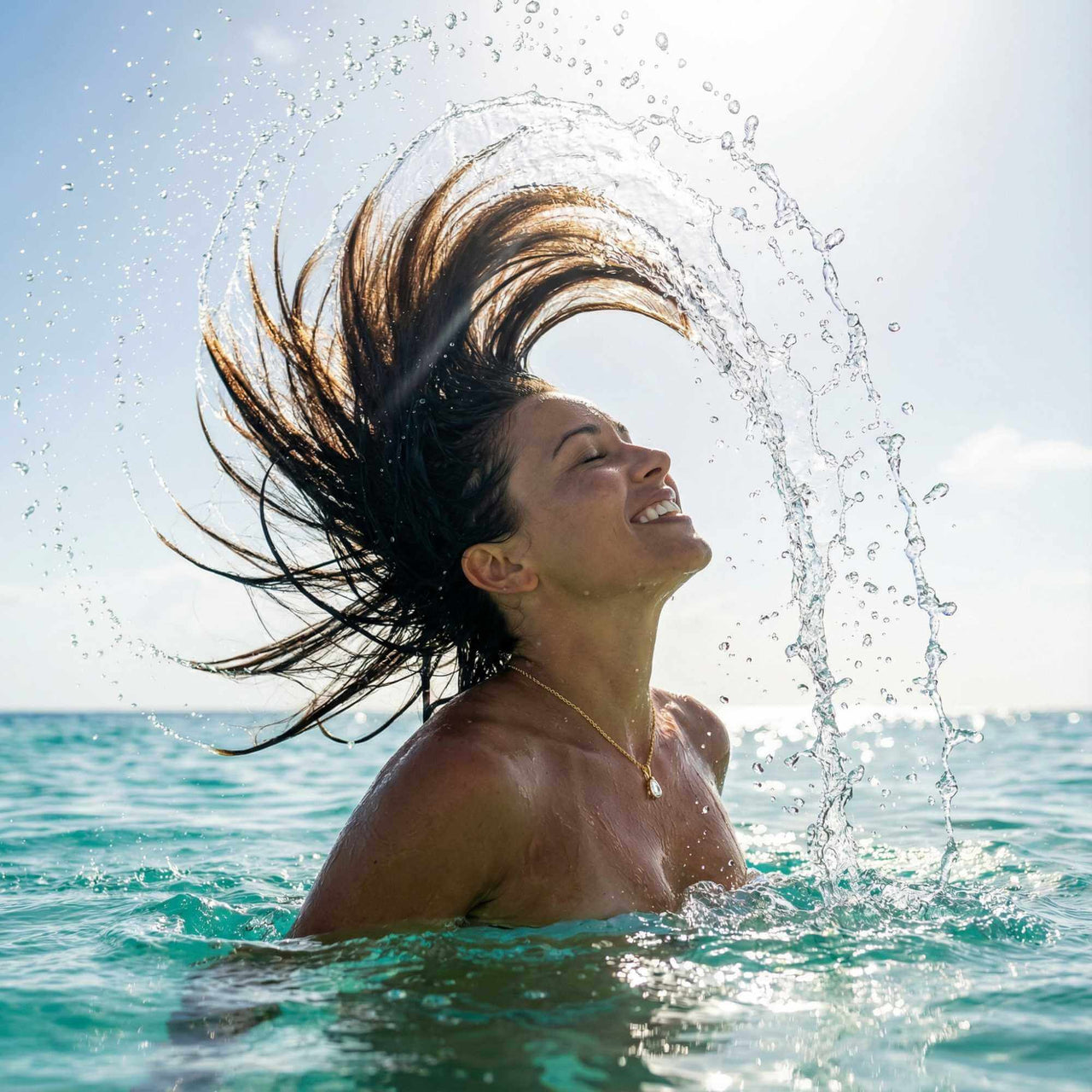 Woman enjoying the ocean with hair splashing water, wearing the Astra Teardrop Necklace by Brother & Sisters.