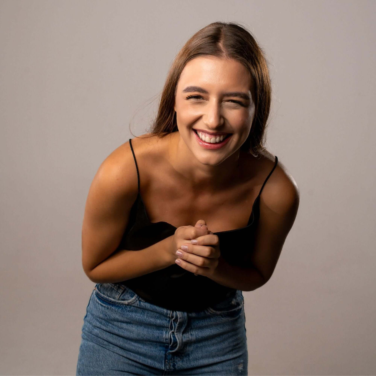 Smiling woman in black top and blue jeans, showcasing happiness in a studio setting.