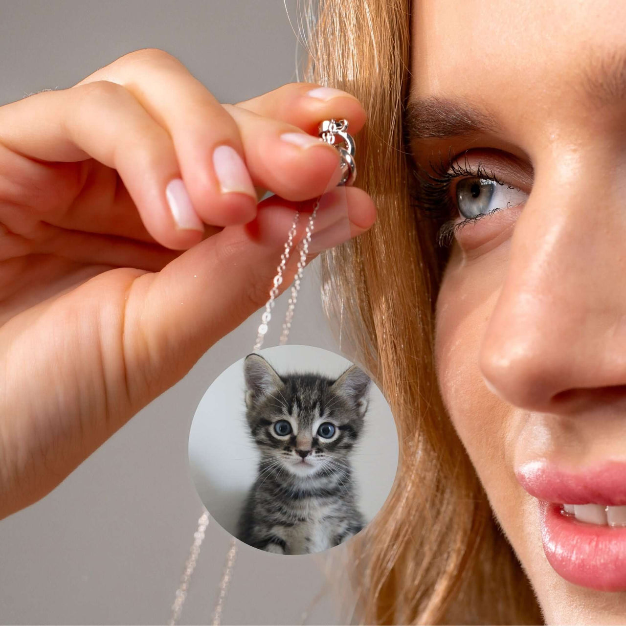 A woman holding the Infinite Photo Necklace featuring a custom photo of a playful kitten by Brother & Sisters.