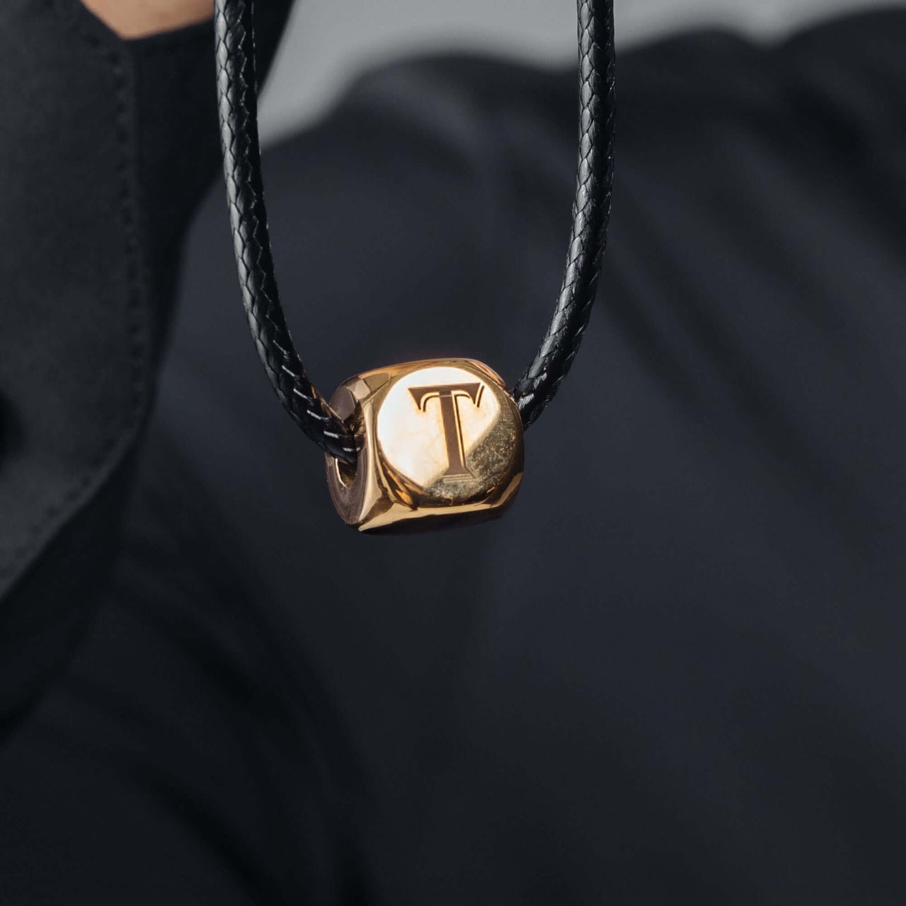Gold Cube Initial Necklace by Brother & Sisters featuring a personalized letter 'T' pendant on a black cord.